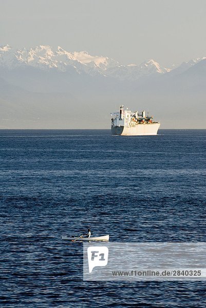 A rower and a Freighter passing through the Strait of Juan de Fuca with Washington's Olympic Mountains in the background  British Columbia  Canada.