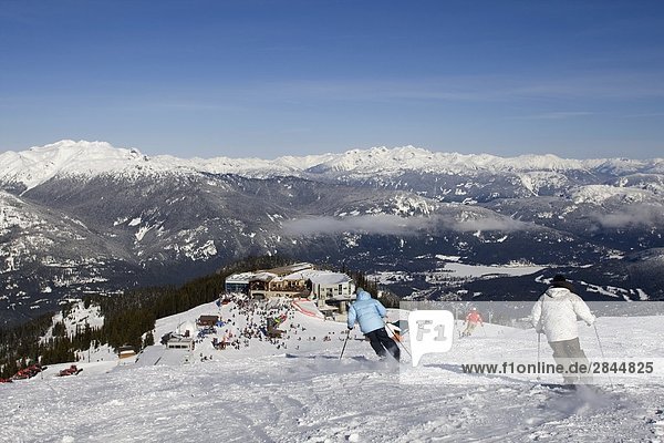Three skiers on slope with Whistler Resort in the background  Whistler  British Columbia  Canada