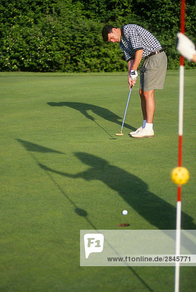 Athletic 20 etwas Golfer Putts Ball  Schatten des Partner auf Gras  Victoria  Vancouver Island  British Columbia  Kanada.
