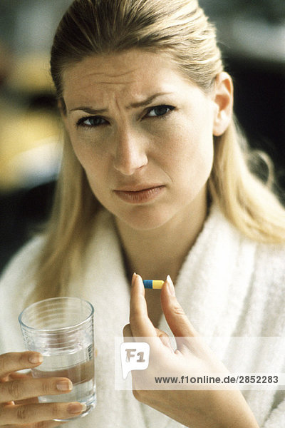 Frau hält Pille und Glas Wasser  Stirnrunzeln vor der Kamera