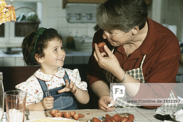 Großmutter und Enkelin zerschneiden Erdbeeren und lächeln sich an.
