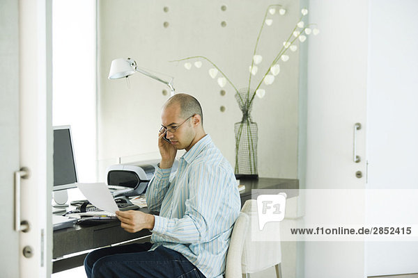 Man working in home office  using cell phone and looking at document
