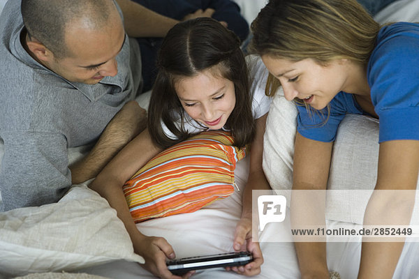Mädchen liegt mit den Eltern  spielt Handheld-Videospiel