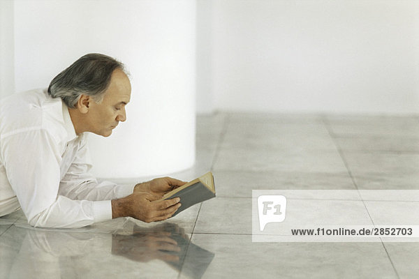 Senior Mann auf gefliestem Boden liegend Lesebuch