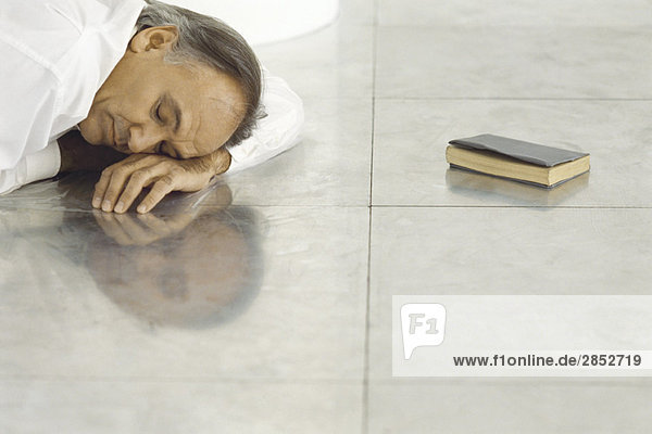 Älterer Mann auf Fliesenboden liegend  Kopf auf dem Arm liegend  schlafend  geschlossenes Buch in der Nähe liegend