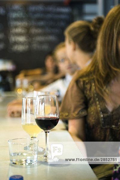 Glasses of wine set on bar  young men and women in conversation in background