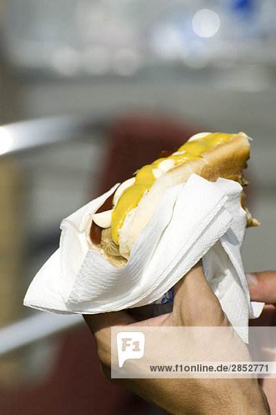 Hand hält Hotdog in Brötchen mit Ketchup und Senf