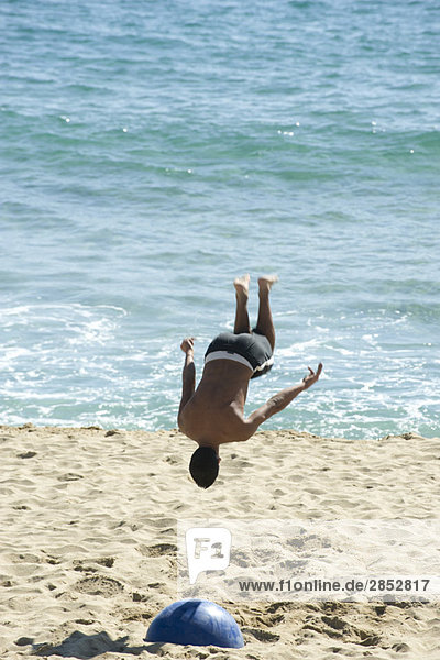 Teenager beim Backflip am Strand