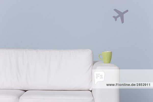 Tasse auf Sofaarm  Flugzeugform im Hintergrund
