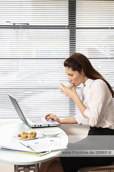 Frau sitzend mit Laptop am Kaffeetisch