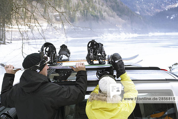 Paar  das Snowboards von Dachgepäckträger nimmt