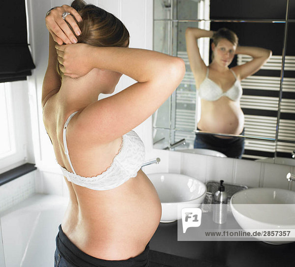 Schwangere Frau schaut in den Spiegel