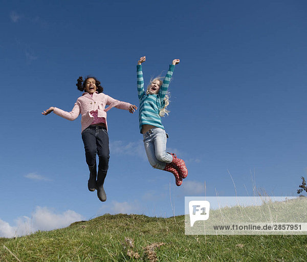 Zwei junge Mädchen springen auf dem Hügel