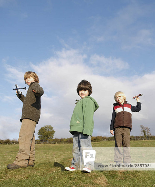 Boys throwing toy planes in field