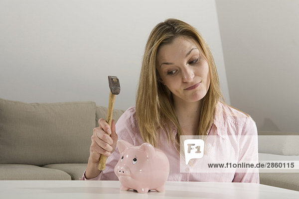 Young woman holding hammer  looking at piggybank