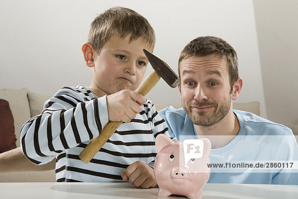Vater und Sohn (4-5) schauen auf Sparschwein  Junge mit Hammer