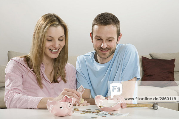 Young couple counting money  broken piggybank on table