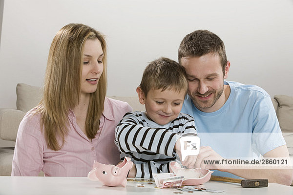 Eltern und Sohn (4-5) schauen auf gebrochenes Sparschwein  zählen Geld