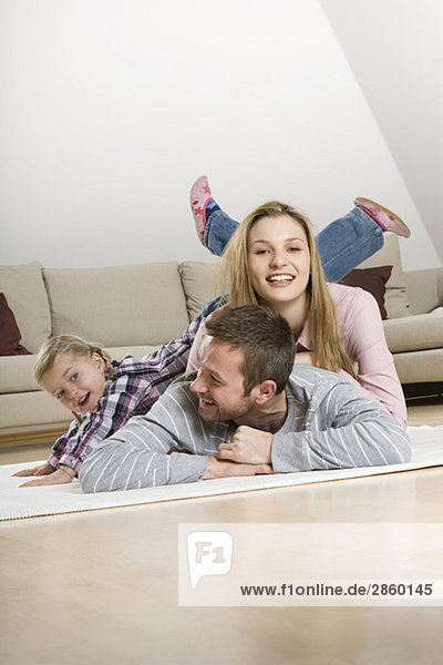 Eltern und Tochter (3-4) zu Hause  auf dem Boden liegend  herumtollend