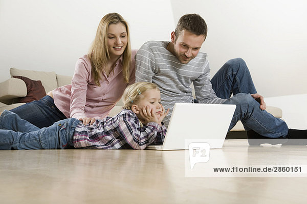 Parents and daughter (3-4) at home  using laptop