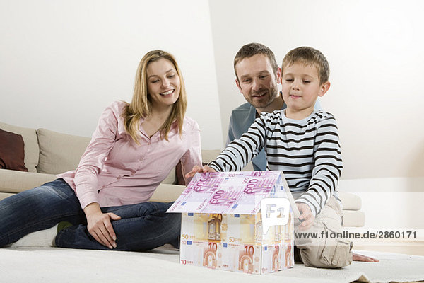 Parents and son (4-5)  building house from Euro notes