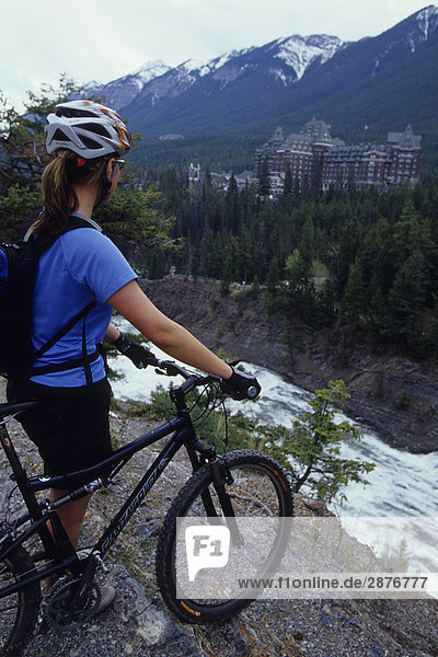 A woman with her mountain bike enjoying the view in Banff National Park  Rocky Mountains  Alberta  Canada. Banff Springs Hotel can be seen in the background.