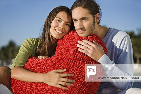 Porträt eines Paares  das sich an ein herzförmiges Kissen schmiegt.