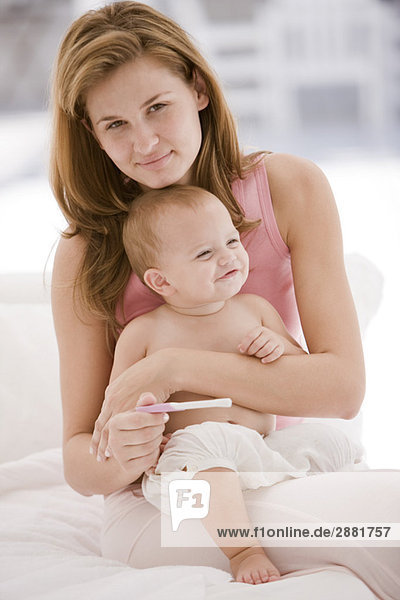 Frau hält einen Schwangerschaftsteststab mit ihrer Tochter auf dem Schoß.