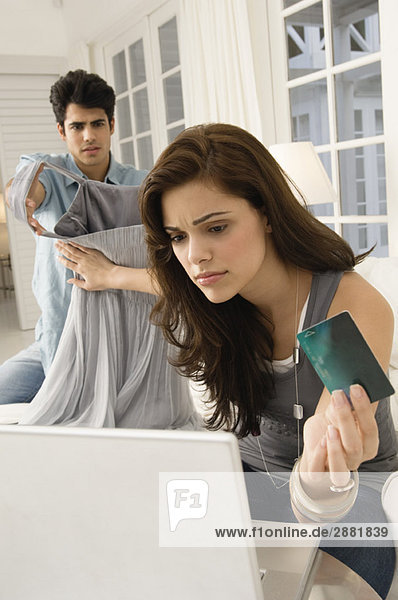 Woman shopping online with a credit card and her husband showing her a dress