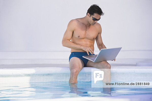 Mann mit einem Laptop am Pool