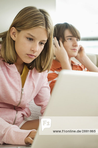 Mädchen arbeiten an einem Laptop und Junge hören Kopfhörer