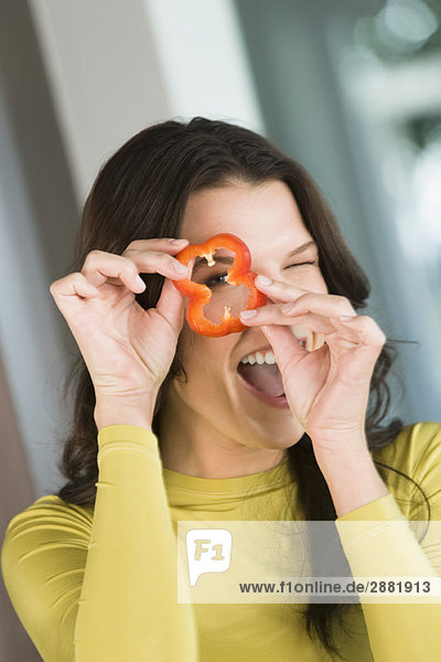 Woman looking through a slice of red bell pepper