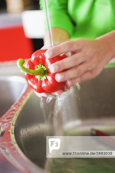 Mid section view of a woman washing a red bell pepper under a faucet