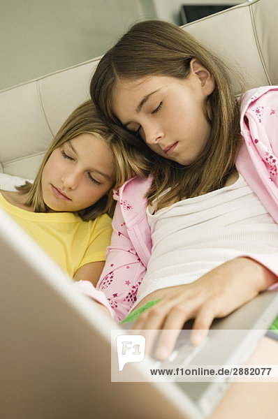 Zwei Mädchen  die mit einem Laptop auf dem Schoß schlafen.