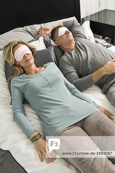 Ein Paar schläft im Bett und trägt eine Augenmaske.