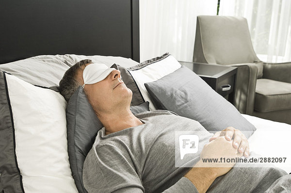 Im Bett schlafender Mann mit Augenmaske