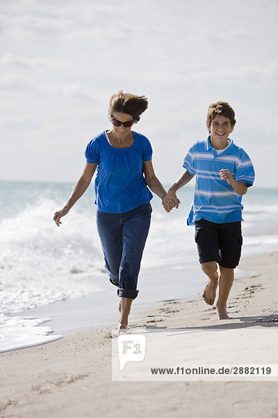Frau läuft mit ihrem Enkel am Strand entlang