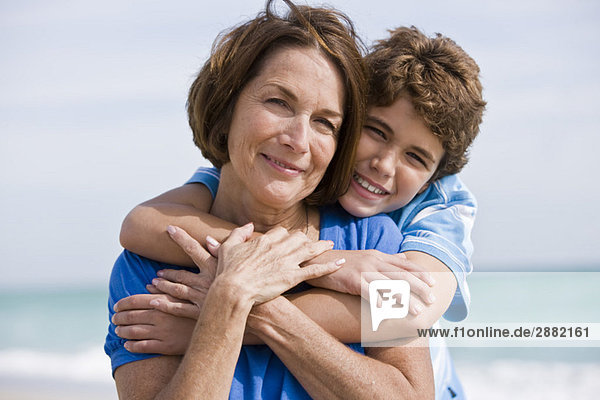 Junge umarmt seine Großmutter am Strand