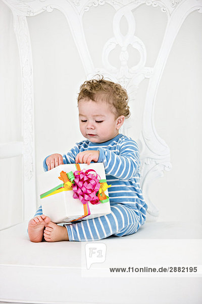 Baby boy playing with a present in an armchair