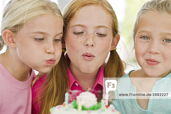 Nahaufnahme von drei Mädchen  die Kerzen auf einer Geburtstagstorte ausblasen.