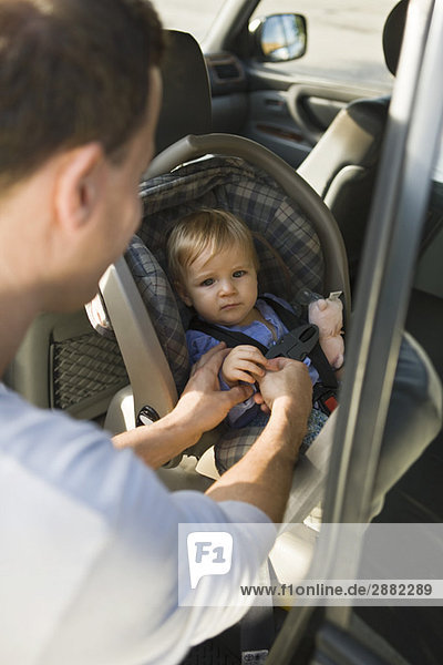 Mann  der seinen Sohn auf einem Kindersitz in einem Auto befestigt.
