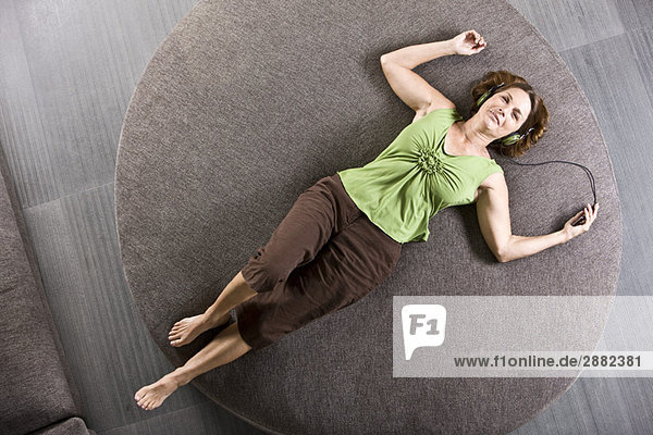 Woman lying on a round sofa and listening to headphones