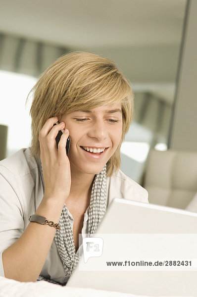 Teenage boy working on a laptop and talking on a mobile phone