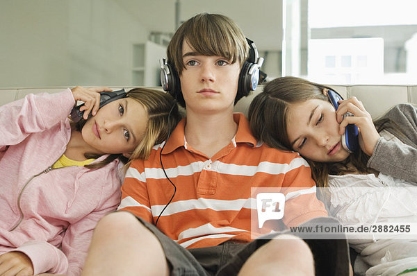 Two girls talking on mobile phones with a boy listening to headphones