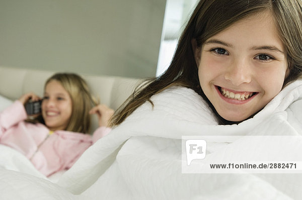Porträt eines Mädchens  das mit seiner Schwester lächelt und im Hintergrund auf einem Mobiltelefon spricht.