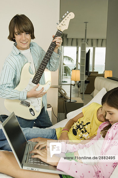 Boy playing a guitar and girl working on a laptop