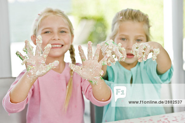 Zwei Mädchen  die ihre Hände mit Kuchenglasur bedeckt zeigen.