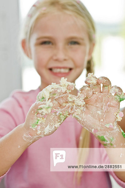 Porträt eines Mädchens  das seine unordentliche Hand mit Kuchenglasur bedeckt zeigt.