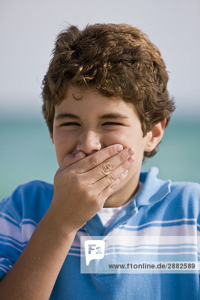 Porträt eines lächelnden Jungen mit bedecktem Mund