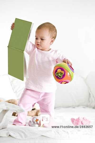 Kleines Mädchen spielt mit einem Bilderbuch und einem Spielzeug